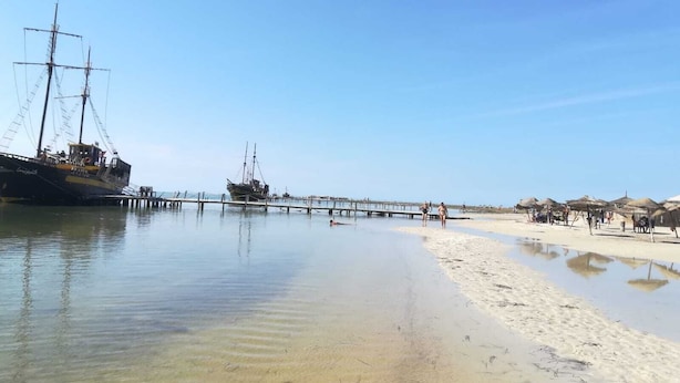 A beach with a ship docked at a pier, clear skies, and a sandy shore. - 'DAR Leyla' CHARMING VILLA WITH POOL.... AT THE HEART OF THE DJERBIAN CAMPAIGN (Mezraya)
