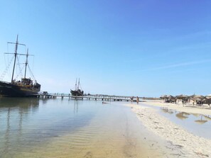 En strand med ett fartyg förtöjt vid en brygga, klar himmel och en sandstrand.