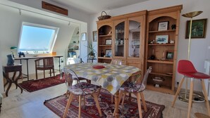 Uma área de refeições com mesa redonda, cadeiras, uma cadeira vermelha, um armário com portas de vidro, um radiador e uma janela com vista.