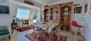 Un comedor con una mesa redonda, sillas, una silla roja, un armario con puertas de vidrio, un radiador y una ventana con vistas.