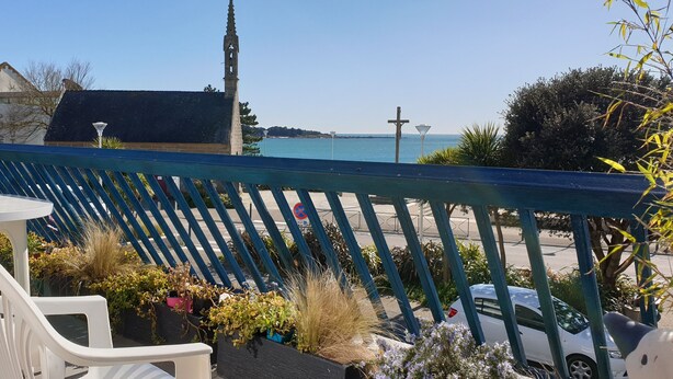 Uma varanda com vista para o mar, uma mesa com cadeiras e plantas em vasos.