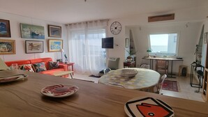 Uma sala de estar aconchegante com uma mesa de jantar de madeira, um sofá vermelho e uma TV fixada na parede.