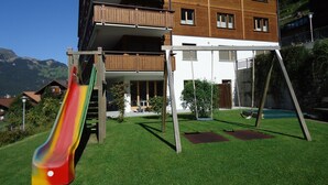 A multi-story building with a balcony, a playground with a slide, and a grassy area. - Chalet Bella Vista 1 (Lauterbrunnen)