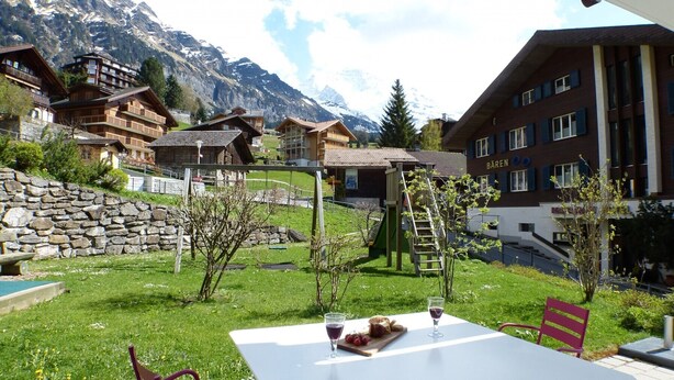 A mountain resort with wooden buildings, a stone wall, and a table with food and drinks. - Chalet Bella Vista 1 (Lauterbrunnen)