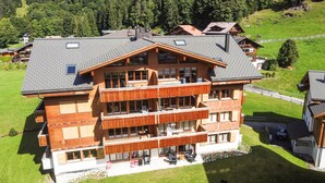 A multi-story building with balconies, a ski slope in the background, and a well-maintained lawn. - Chalet Aquila 7 Penthouse (Lauterbrunnen)