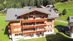 A multi-story building with balconies, a ski lift in the background, and a green landscape.