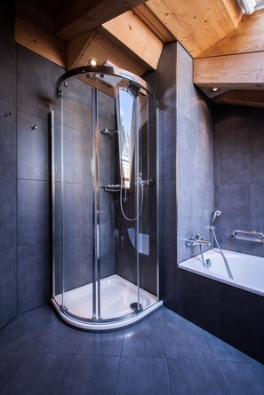 A modern bathroom with a glass-enclosed shower, a standalone bathtub, and dark tiled walls. - Chalet Aquila 7 Penthouse (Lauterbrunnen)