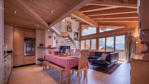 A spacious living area with a dining table set for four, a sofa, and a staircase leading to an upper level. - Chalet Aquila 7 Penthouse (Lauterbrunnen)