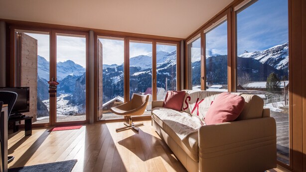 A modern living room with a large window offering a mountain view, a sofa with decorative pillows, and a wooden floor. - Chalet Dillon (Lauterbrunnen)