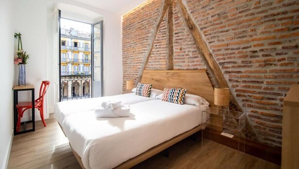 Ein modernes Hotelzimmer mit einem großen Bett, einer Wand aus Ziegelsteinen und Blick auf Gebäude durch eine Glastür.
