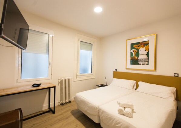A hotel room with a bed, a desk, a television, and a framed picture on the wall. - Central Roomss (San Sebastián)