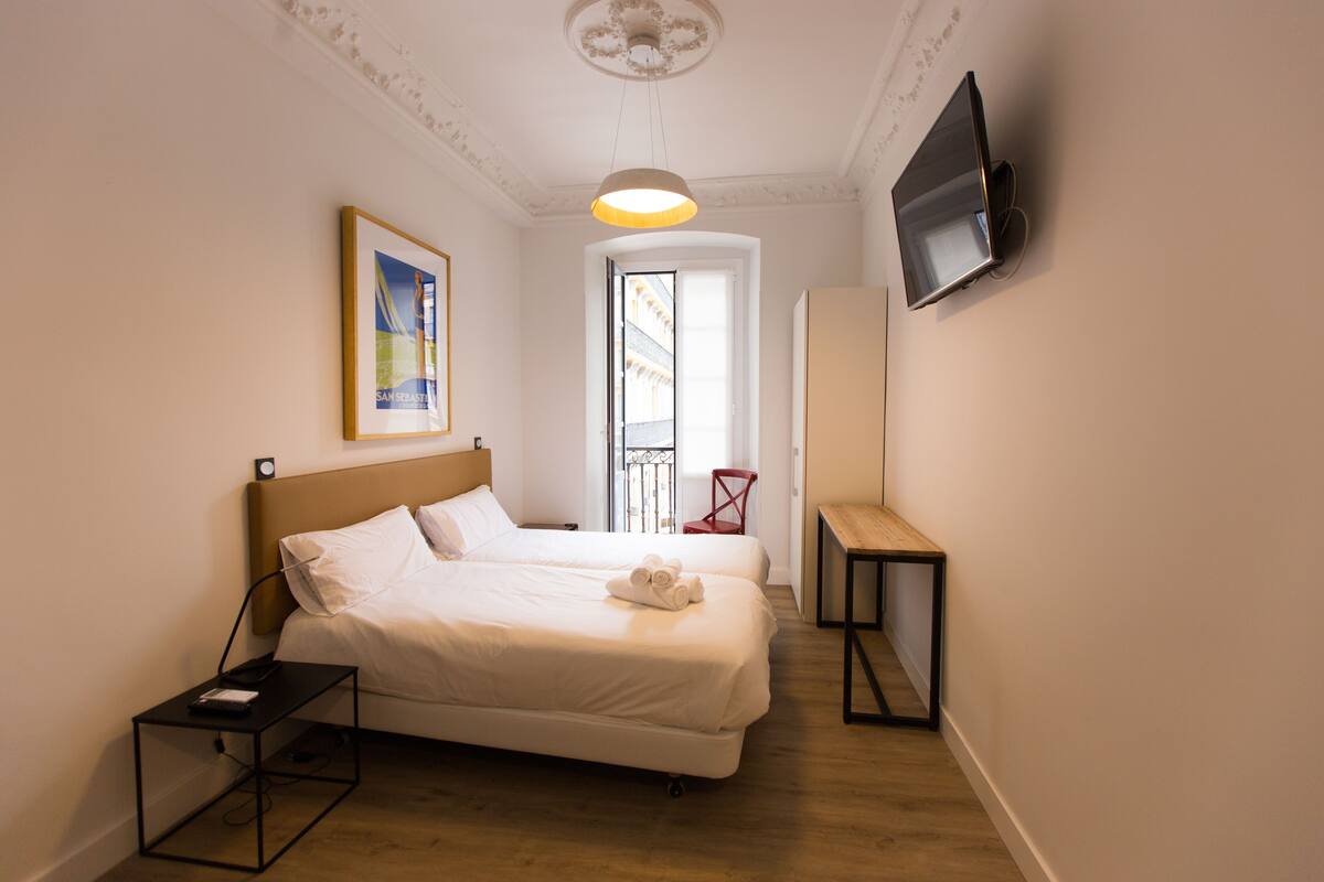 Hotellihuone, jossa on kaksi sänkyä, seinälle asennettu televisio, pieni pöytä ja tuoli.