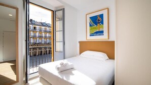 Ein Hotelzimmer mit Bett, einem gerahmten Poster und einem Balkon mit Blick auf ein Gebäude.