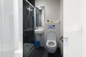 A modern bathroom with a glass shower enclosure, a white sink, and a toilet. - Central Roomss (San Sebastián)