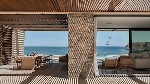A modern outdoor seating area with a view of the sea, featuring a stone pillar, wicker furniture, and a clear sky.