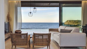 Een moderne woonkamer met uitzicht op zee, met een bank, twee rieten stoelen, een eettafel en hanglampen.