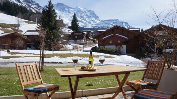 A patio with a table, two chairs, and a bottle of wine. - Chalet Brunner 3 (Lauterbrunnen)