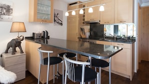A modern kitchen with a central island, bar stools, wooden cabinets, and a built-in oven. - Chalet Brunner 3 (Lauterbrunnen)
