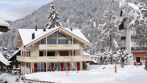 A two-story chalet with a balcony, surrounded by snow-covered trees and a mountain backdrop. - Chalet Brunner 3 (Lauterbrunnen)