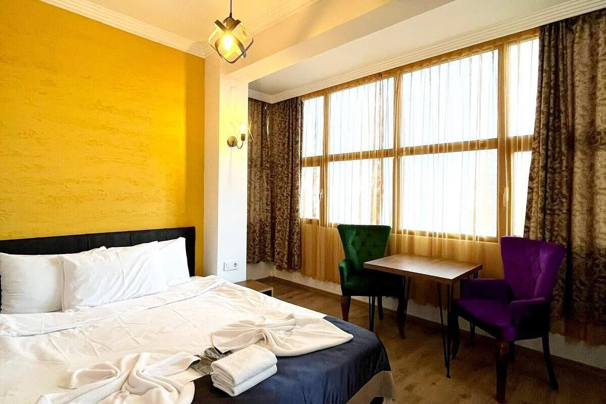 Ein Hotelzimmer mit einem Bett, einem Schreibtisch, zwei Stühlen, einem Vorhangfenster und einer Pendelleuchte.