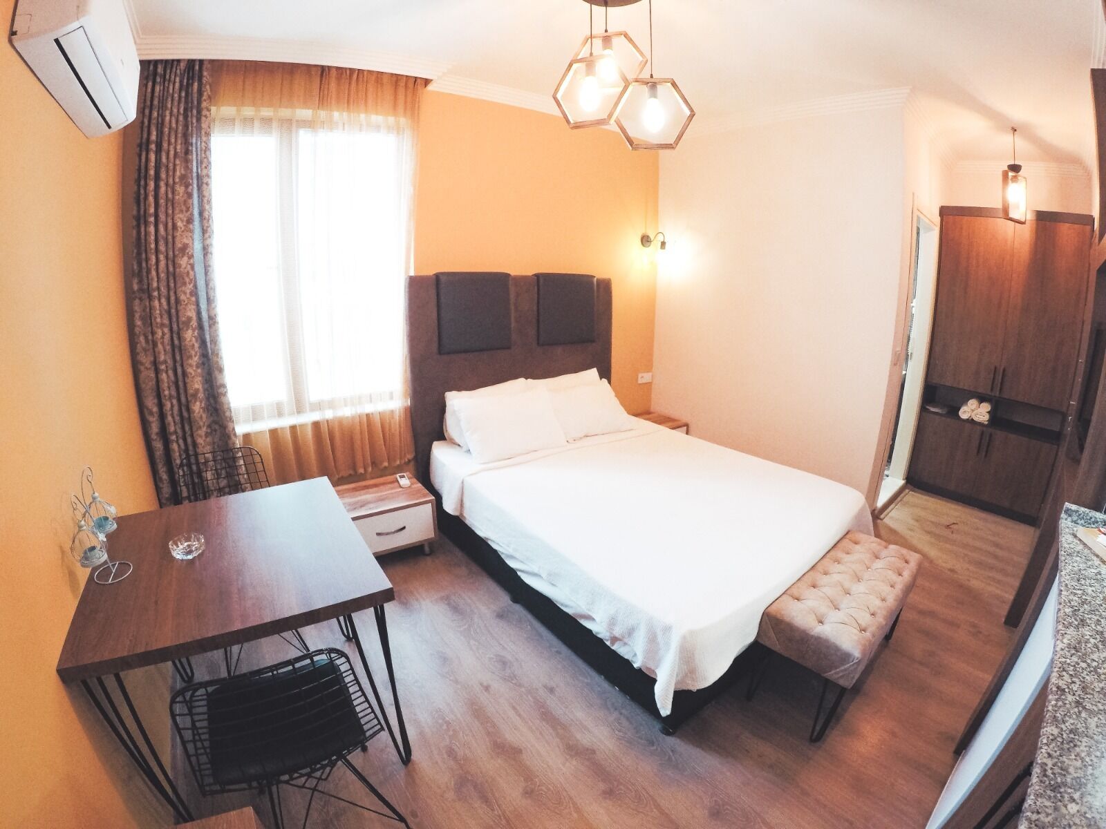 A hotel room with a bed, bedside table, chair, desk, and wardrobe.