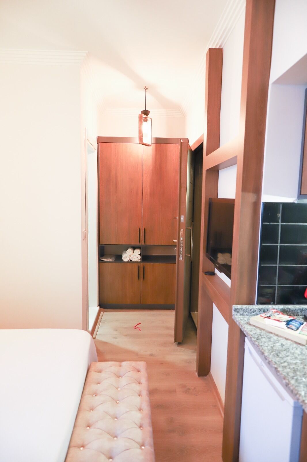 A narrow hallway with a wooden wardrobe, a bench, and a kitchen area with a granite countertop.