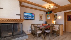A dining area with a stone fireplace, wooden ceiling beams, and a television mounted on the wall. - Chalet Bergkristall (Lauterbrunnen)