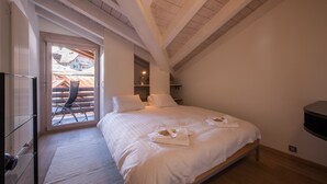 A bedroom with a large bed, a chair by the window, and a view of the outside buildings.