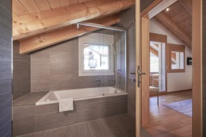 A modern bathroom with a freestanding bathtub, a glass shower enclosure, and a large mirror above the tub. - Chalet Bergfrieden Penthouse (Lauterbrunnen)