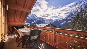A wooden balcony with a table and chairs, overlooking snow-capped mountains.
