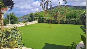 Una cancha de tenis con red, rodeada de exuberante vegetación y un muro de piedra.