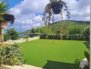 Una cancha de tenis con red, rodeada de exuberante vegetación y un muro de piedra.