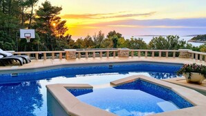 Una piscina de diseño curvo, rodeada de sillones de descanso y un aro de baloncesto.
