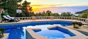 Una piscina de diseño curvo, rodeada de sillones de descanso y un aro de baloncesto.