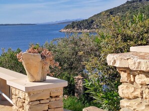 Une balustrade en pierre surplombe un paysage côtier, offrant une vue dégagée sur la mer et les collines lointaines.