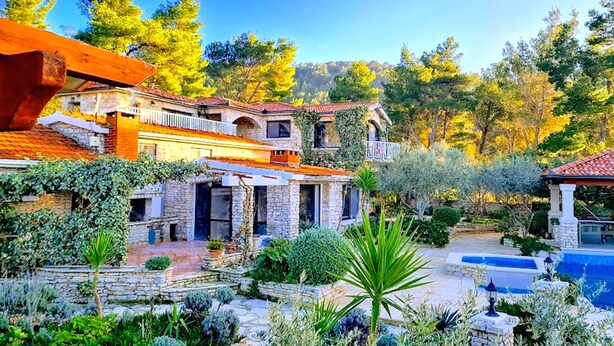 Una casa de piedra tradicional con un patio de piedra, piscina y abundante vegetación.