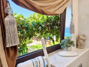 Ein Zimmer mit Meerblick, ein Fenster mit Vorhängen, eine Pflanze, eine Statue und ein weißer Tisch.