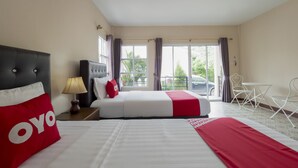 Une chambre d’hôtel avec un grand lit, une table de chevet, une lampe, une fenêtre avec des rideaux, un balcon et un coin repas avec des chaises.