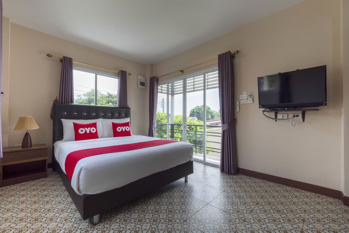 A hotel room with a large bed, a TV mounted on the wall, and a balcony with curtains.