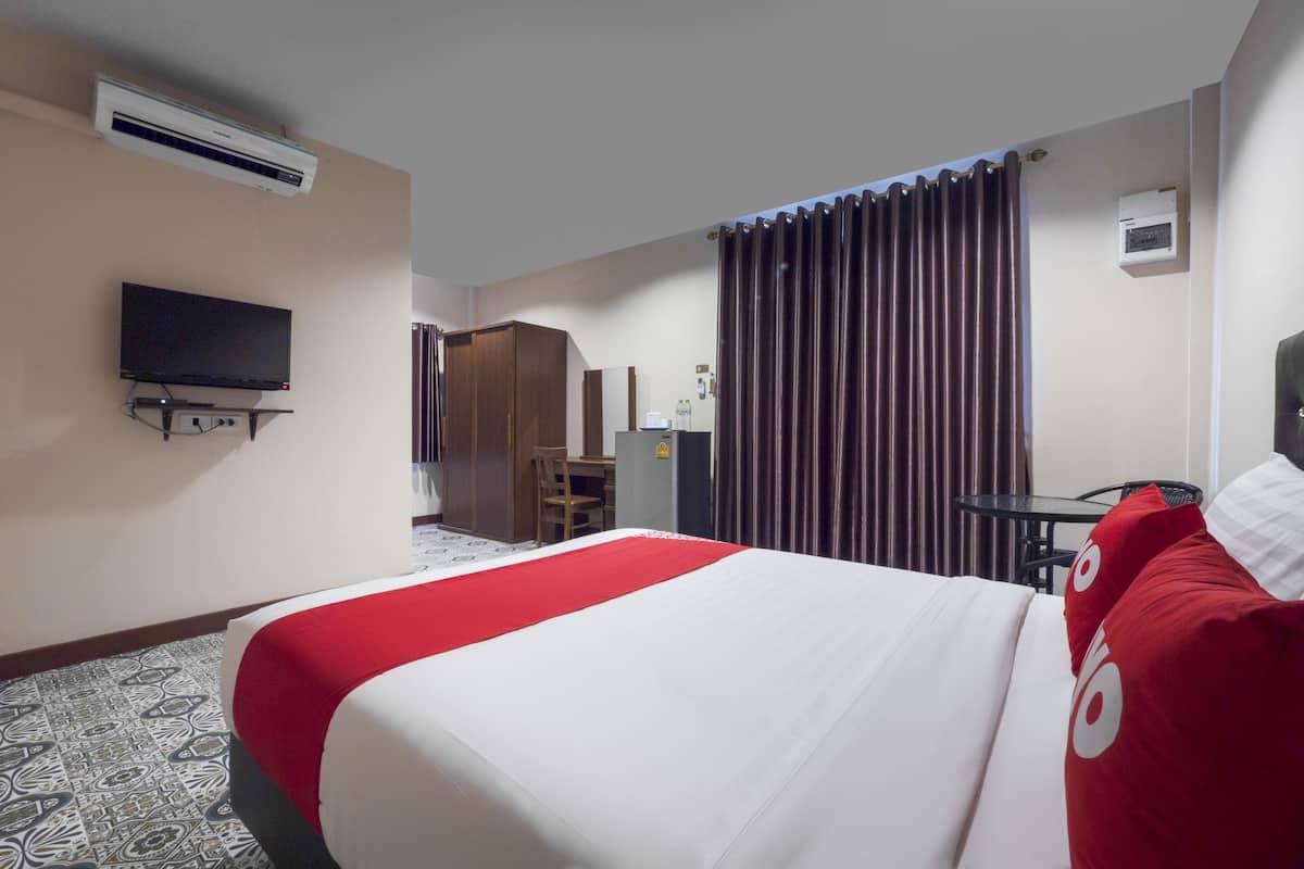 A hotel room with a bed, a television, a desk, and a window with curtains.