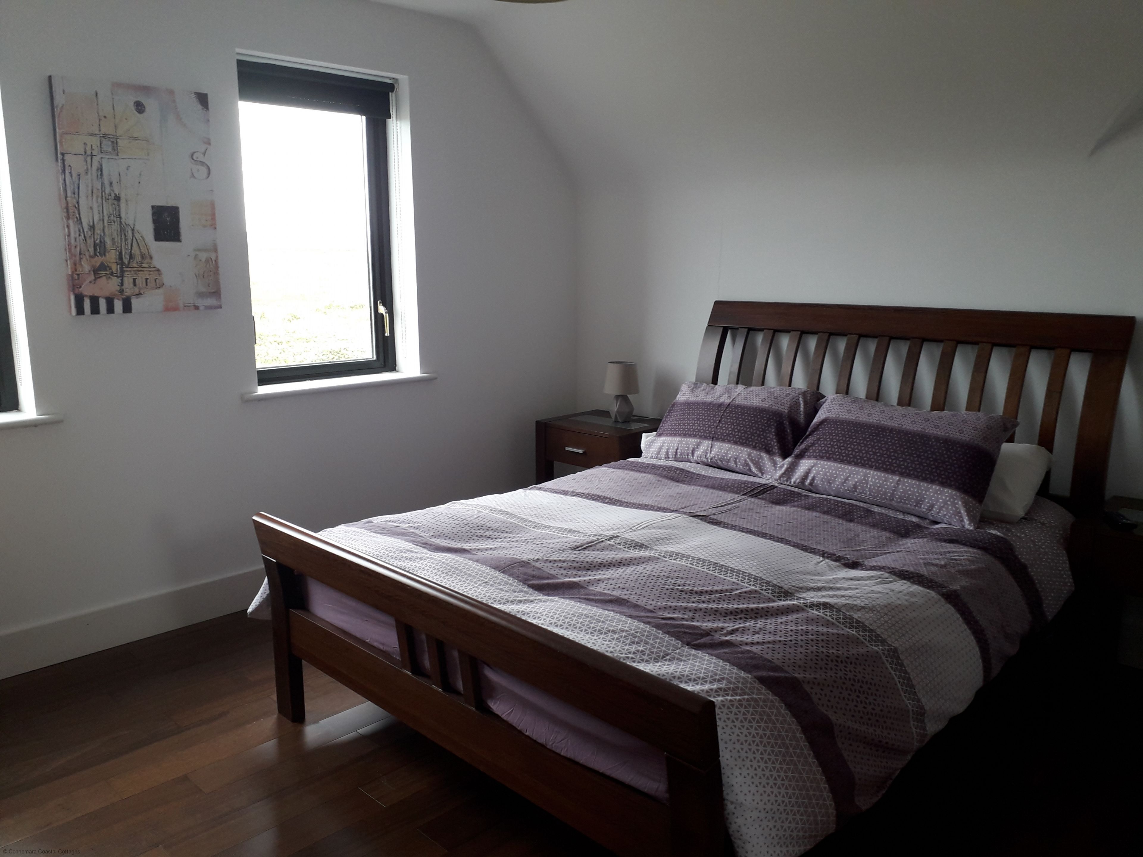 A bedroom with a wooden bed, a nightstand, a window with a view, and a wall with artwork.