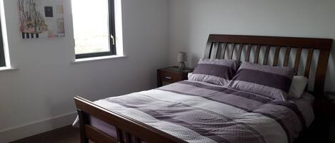 A bedroom with a wooden bed, a nightstand, a window with a view, and a wall with artwork.