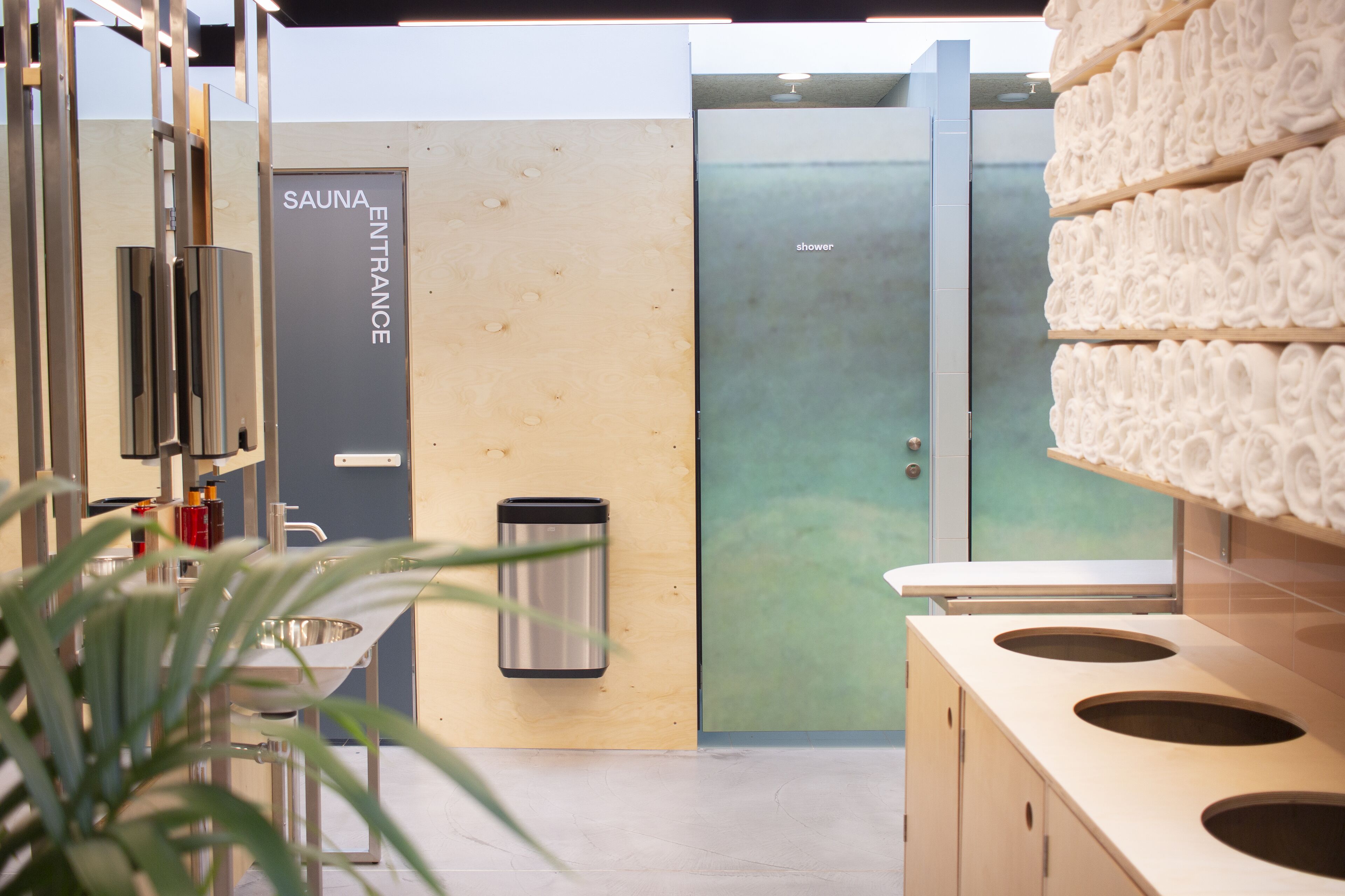 A modern bathroom with a sauna entrance sign, a sink, a trash bin, and a towel rack.