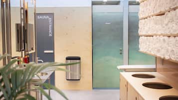 A modern bathroom with a sauna entrance sign, a sink, a trash bin, and a towel rack.