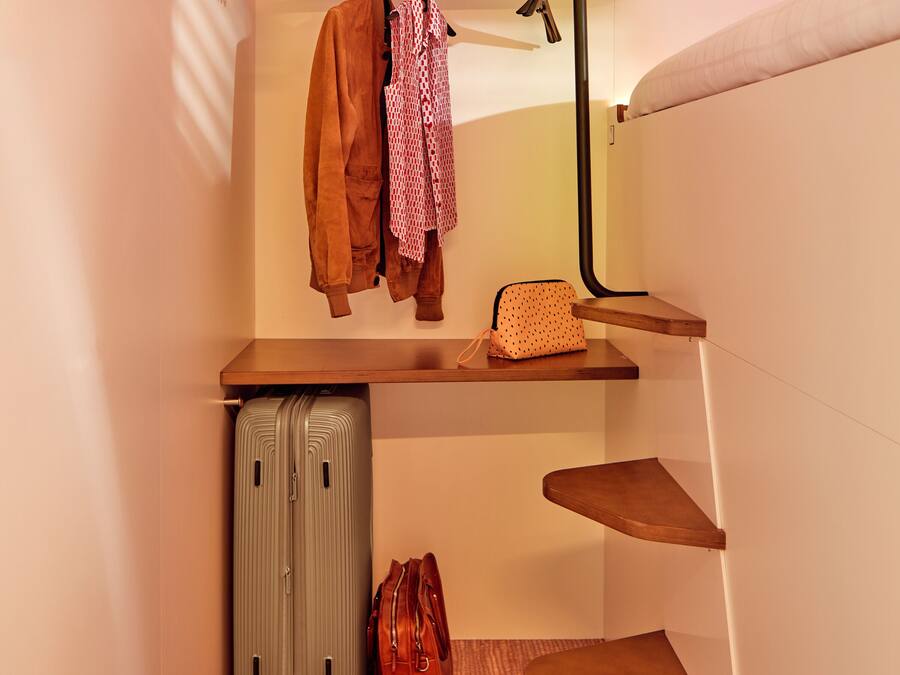 A compact hotel room with a built-in bench, a suitcase, a pair of shoes, and a handbag.