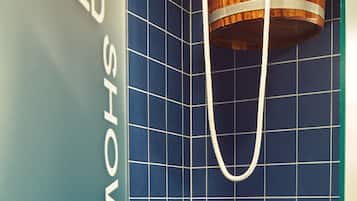 Un baño con pared de azulejos azules, un cubo de madera colgado de un gancho metálico y un letrero que dice 'COLD SHOWER'.