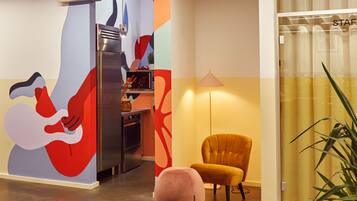 A modern kitchen with a stainless steel refrigerator, a dining area with a yellow chair, and a wall with abstract art.