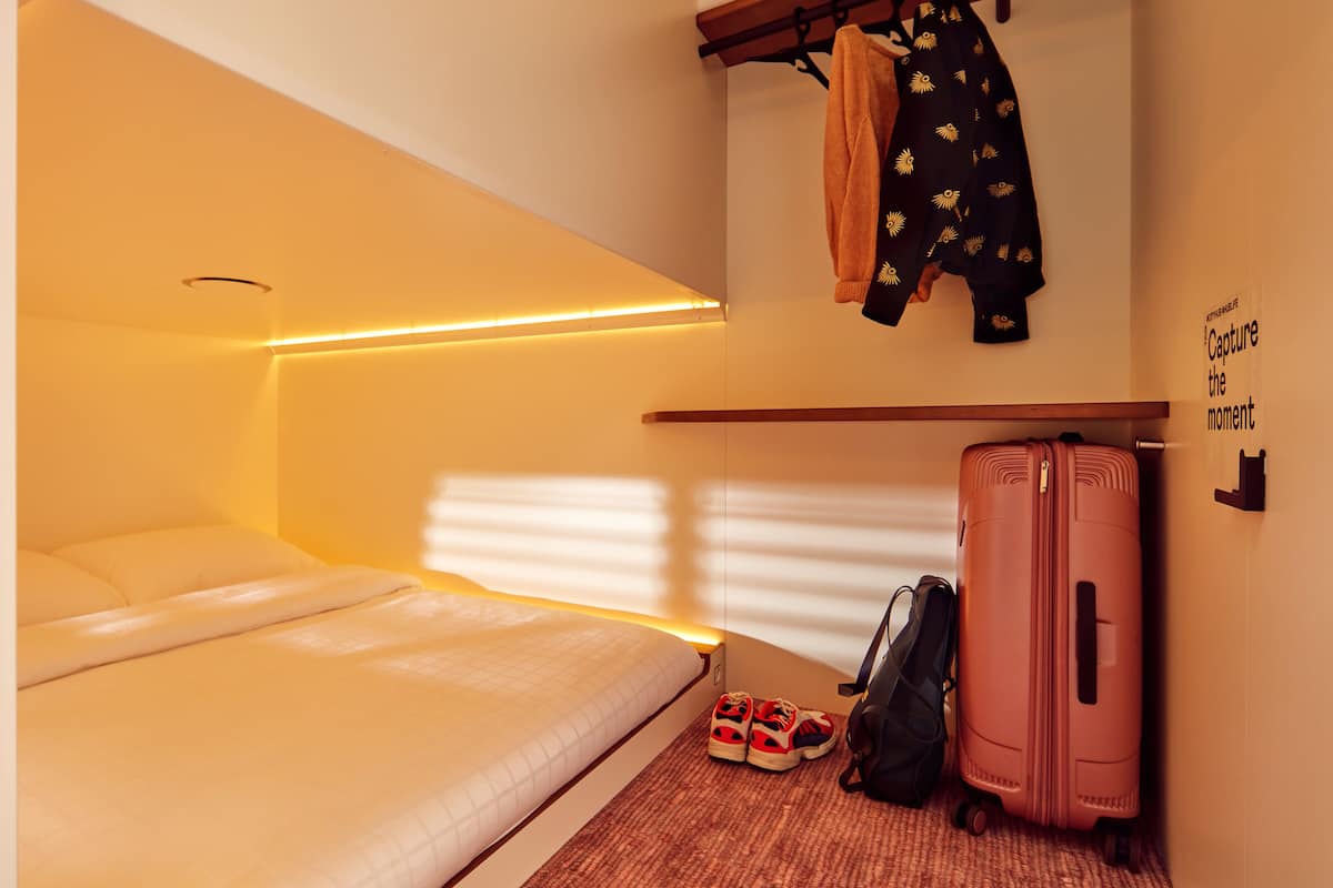 Un dormitorio con una cama, una maleta y una chaqueta colgada en la pared.