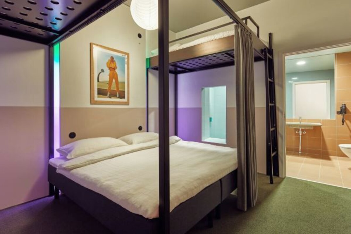 Una habitación con una cama, un cuadro en la pared y un baño visible a través de una puerta abierta.