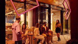Un groupe de personnes est assis et se tient debout devant un bâtiment sur lequel on peut lire l’inscription « City Hub ».